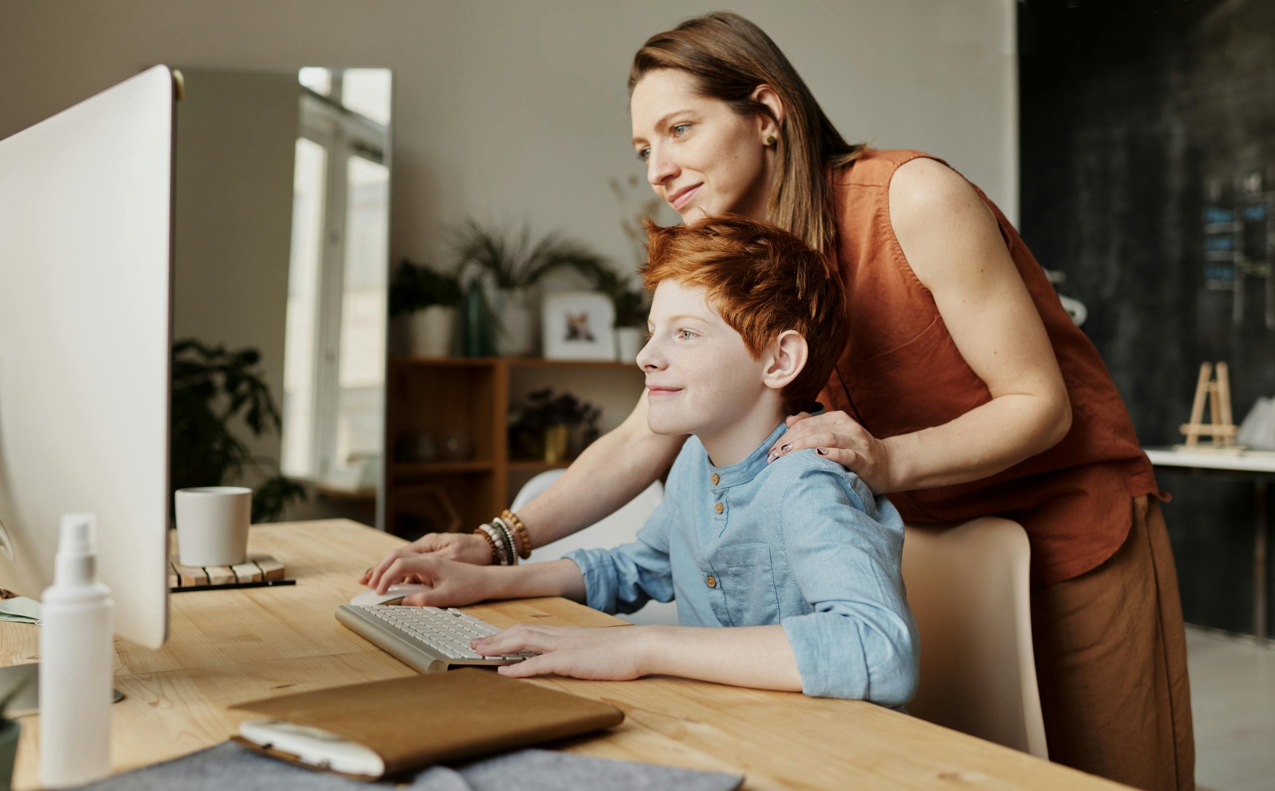 A mother and her child smiling while using a computer at home, focused on learning.